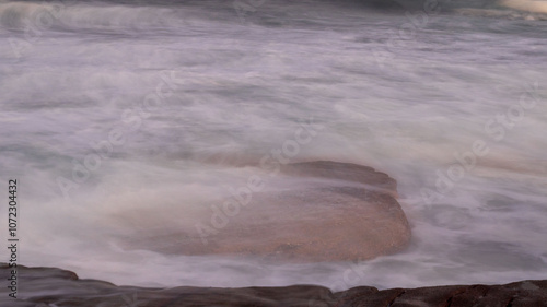 Slow shutter speed photo of ocean water flowing over a rock, located at orange rocks in Margate South Africa