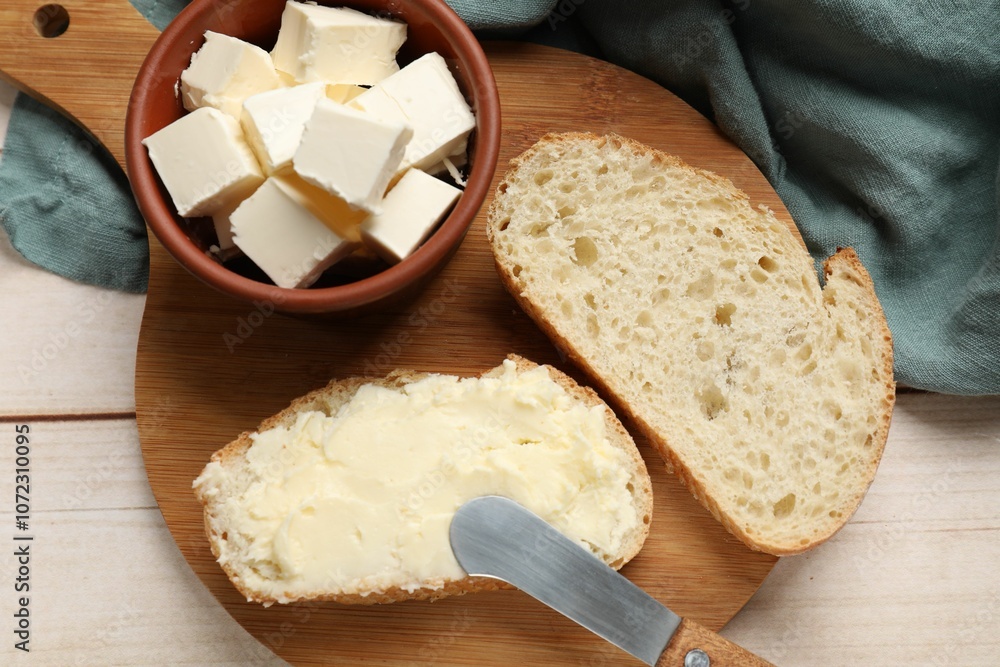 Fresh bread with butter and knife on light wooden table, top view