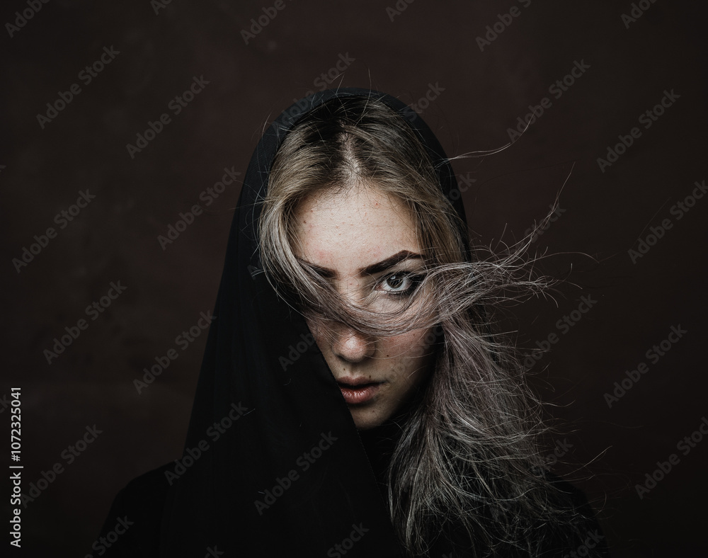 Emotional portrait of a girl with a covered head on a dark background