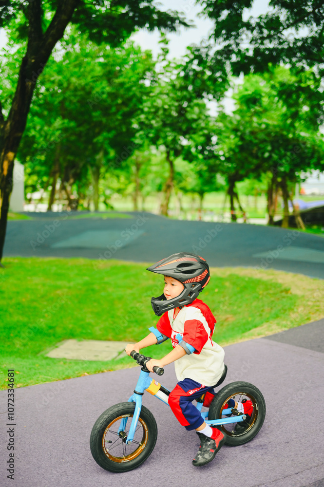 4 years old boy in safety helmeriding balance bike at summer park green trees enjoy happy childhood. .Kids on bicycle in sunny park. Sport for kids.