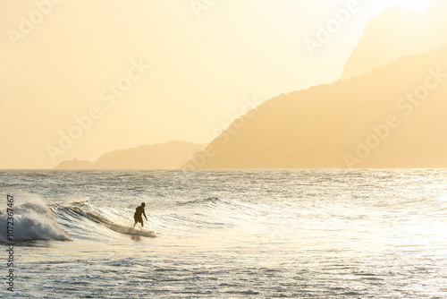 Surfer riding the waves in front of scenic hills at Ipanema Beach in Rio de Janeiro in Brazil at sunset