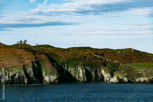 Coastal cliff landscape with rugged rocks and trees near the water during daylight at a scenic location. photo