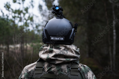 Military instructor in a helmet with a night vision device in the forest at dusk. View from the back. photo