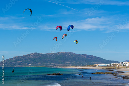 Unrecognized people kitesurfing at the beach with cityscape and mountain in the background in Tangier, Morocco.