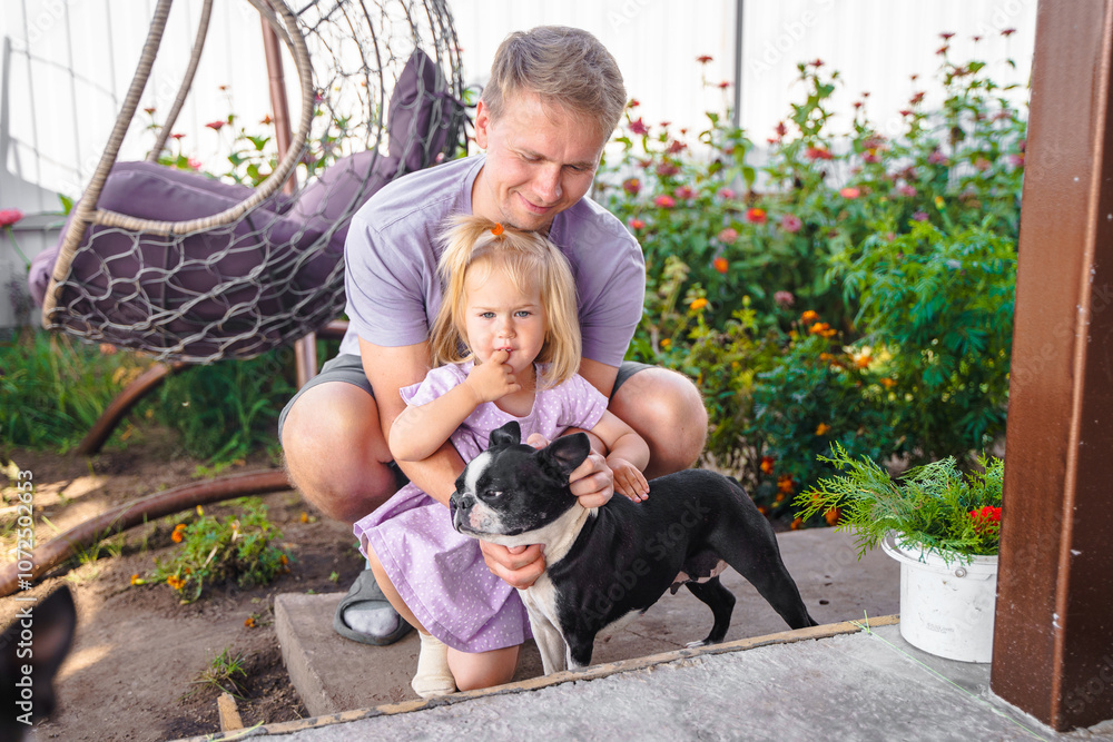 Little child girl with father petting and hugging a Boston terrier dog outside. A family dog, caring and loving for animals. Little child girl with father petting and hugging a Boston terrier dog outside. A family dog, caring and loving for animals.