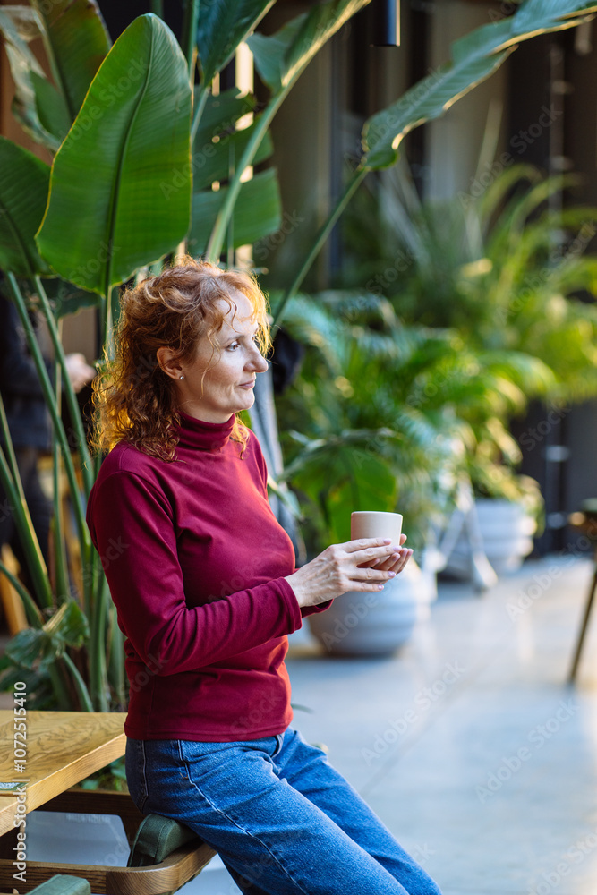 Fototapeta premium Relaxed woman enjoying coffee in indoor garden setting