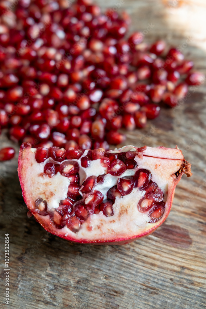 cut piece of fresh pomegranate on a wooden table, against a background of red seeds cut piece of fresh pomegranate on a wooden table, against a background of red seeds