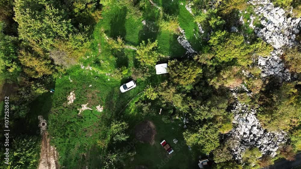 A small white passenger car with a trailer - mobile home is parked at a camping site in a green clearing. Aerial top view from drone. Travel, adventure and road trip concept A small white passenger car with a trailer - mobile home is parked at a camping site in a green clearing. Aerial top view from drone. Travel, adventure and road trip concept