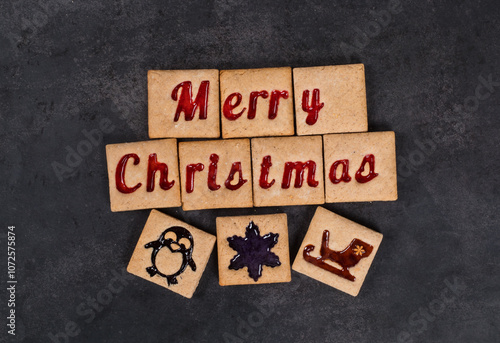 Merry Christmas. Ginger square cookies with colored marmalade filling in the shape of the words Merry Christmas and sledge, penguin, snowflake. Dark background. Top view