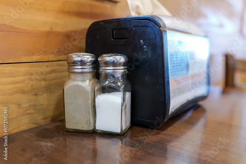 Obraz na płótnie Salt and Pepper shakers next to a napkin dispenser on a wooden cafe table. w salonie