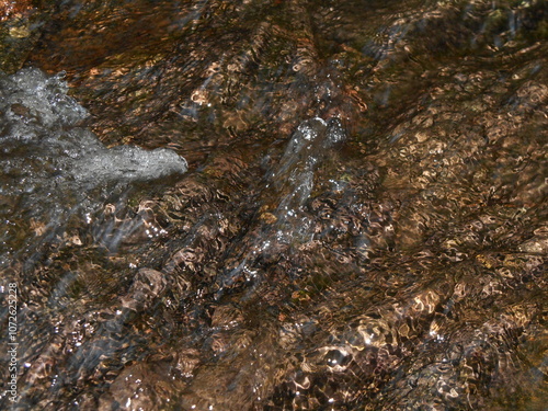 Water in a mountain stream, slightly turbid, with light reflections, brown color. Close-up of water, can be a background, texture or pattern.