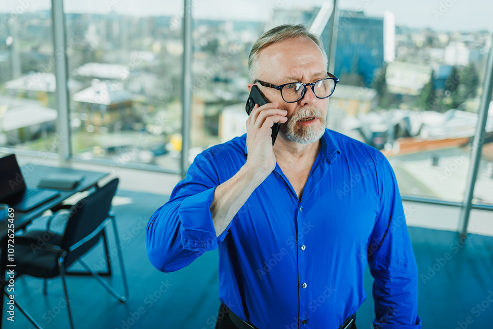 A bearded old man in a shirt works in the office and talks on the phone. A businessman in glasses with a phone in his hands A bearded old man in a shirt works in the office and talks on the phone. A businessman in glasses with a phone in his hands