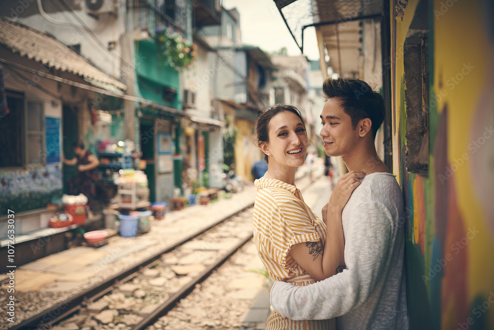 Fototapeta premium City, tramway and couple in portrait on vacation, travel adventure and exploring for anniversary. Interracial marriage, woman and man with smile for admiration, hug and bonding outdoor in Vietnam