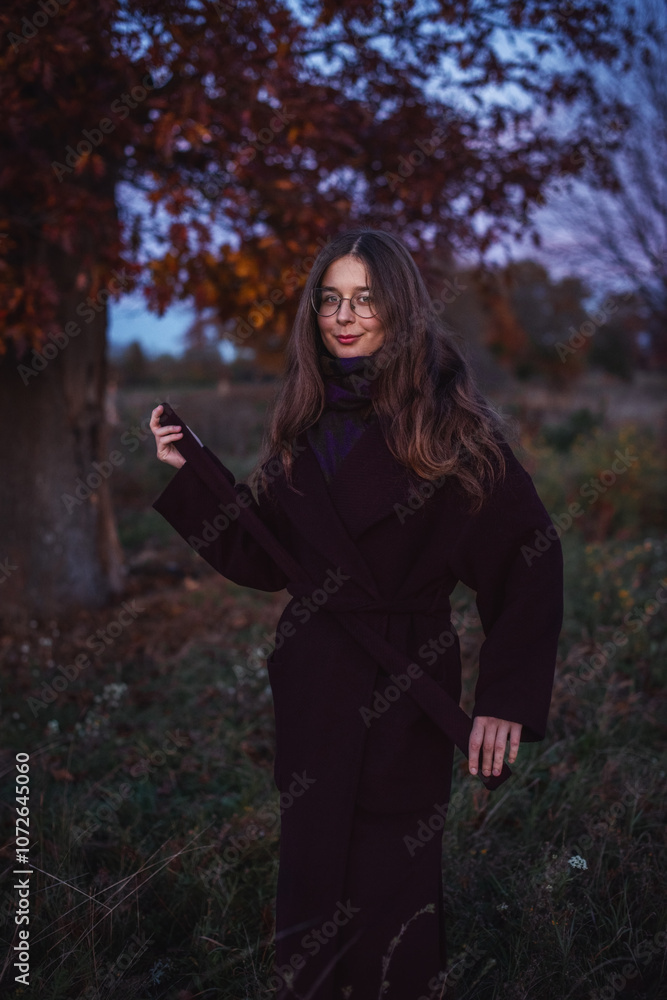 Vertical portrait of a young girl in a burgundy coat against the background of an evening autumn park. Vertical portrait of a young girl in a burgundy coat against the background of an evening autumn park.