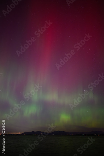 Aurora Borealis Northern Lights with red pillar and green waves over water photo