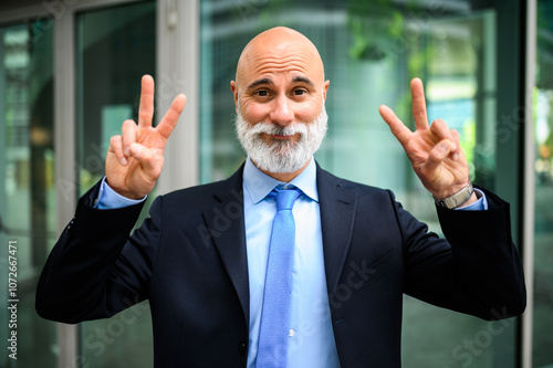 Mature businessman with beard smiling and making victory signs in a contemporary urban environment