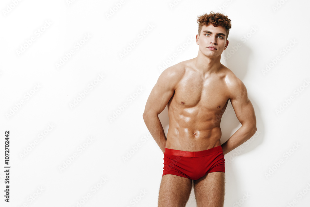 Confident young athletic man posing in red swimwear against a plain white background, showcasing a fit physique and relaxed expression. Fitness and modeling concept. Confident young athletic man posing in red swimwear against a plain white background, showcasing a fit physique and relaxed expression. Fitness and modeling concept.
