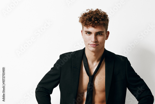 Confident young man with curly hair in an unbuttoned black blazer and loosened tie, posing against a plain white background. Fashion and style concept. photo