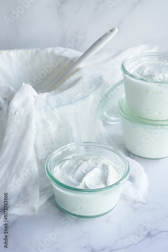 homemade greek style yogurt in a glass bowl on white marble table.