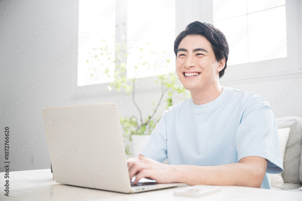 明るい部屋でパソコンを使う笑顔の若い男性 フリーランスやエンジニア、デザイナーなどの仕事をする人の爽やかな見上げるイメージ 明るい部屋でパソコンを使う笑顔の若い男性 フリーランスやエンジニア、デザイナーなどの仕事をする人の爽やかな見上げるイメージ