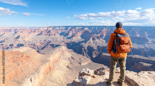 A person stands at edge of breathtaking canyon, gazing at vast landscape of layered rock formations and dramatic cliffs under clear blue sky. scene evokes sense of adventure and awe