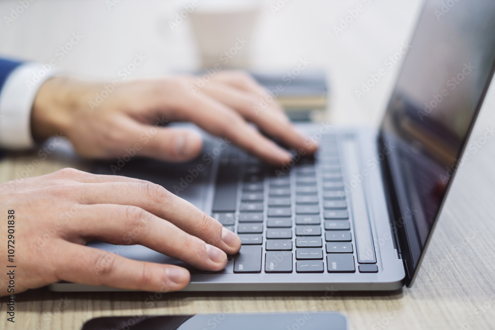 Set against a blurry office setting, a close-up reveals a man's hands typing on a sleek laptop keyboard Set against a blurry office setting, a close-up reveals a man's hands typing on a sleek laptop keyboard