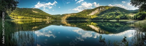 Calm water reflections at a serene lake surrounded by lush green hills under a bright blue sky during midday