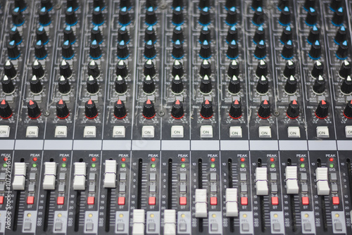 close-up view of an audio mixing console. The console features multiple rows of knobs and sliders. photo