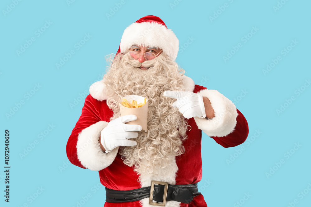 Santa Claus pointing at tasty french fries on blue background Santa Claus pointing at tasty french fries on blue background