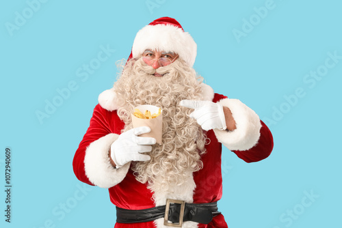 Santa Claus pointing at tasty french fries on blue background