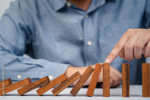 A person stabilizing wooden dominoes with their finger, symbolizing the balance and chain reaction concept. photo