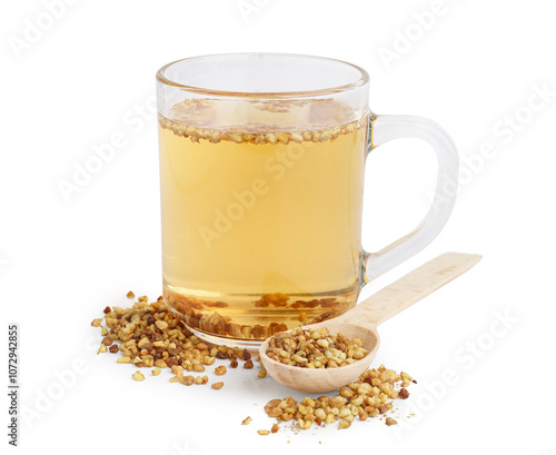 Glass cup of fresh buckwheat tea and wooden spoon on white background