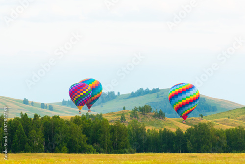 Colorful hot air balloons flying over the green hills and trees at sunset.