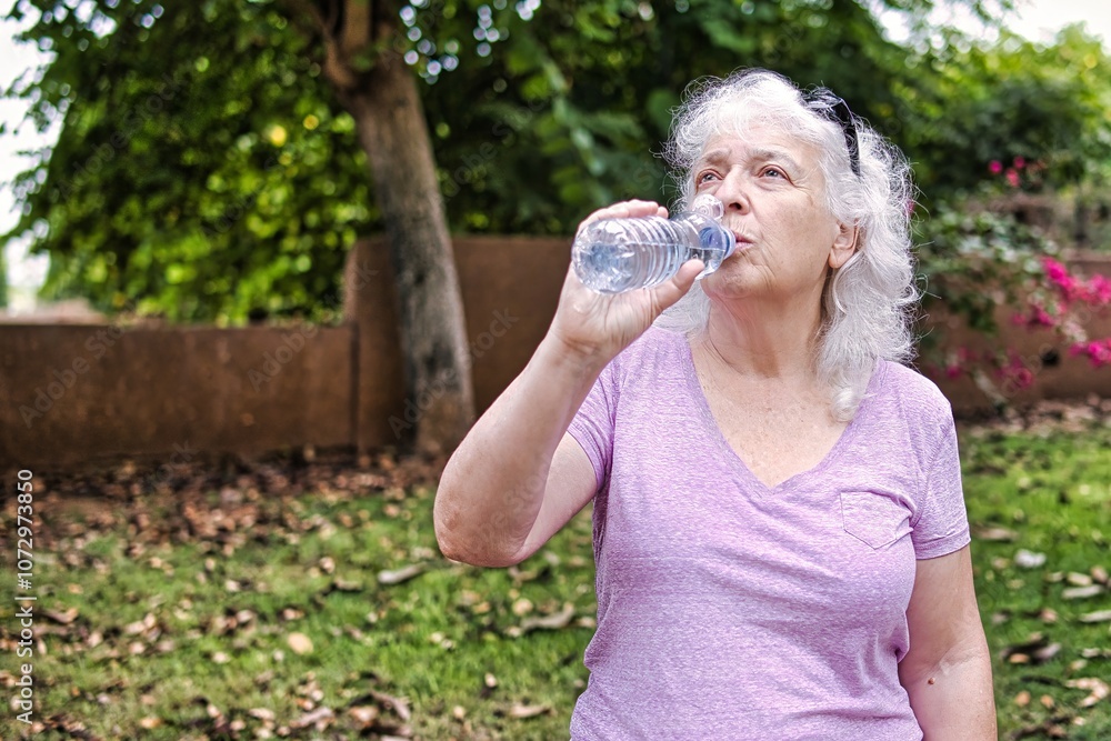 Gray-haired elderly lady drinks water from a bottle in the park. Gray-haired elderly lady drinks water from a bottle in the park.