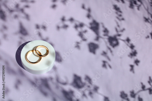 mockup wedding. two gold rings on a white platform on a violet background with penumbra.