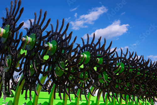 Close-up of a rotary harrow green color for processing an agricultural field. Against the background of the blue sky with clouds.