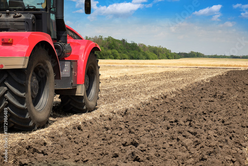 Fototapeta Rear view of a large tractor red color standing in a field