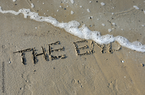 words the end written on a beach with a wave about to erase them photo