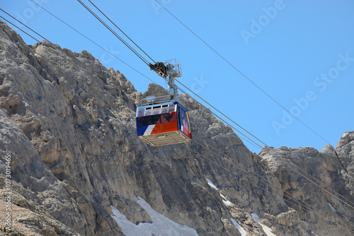 cabin on ropeway on steel ropes to reach the mountain top with alpine rocks and snow in the background
