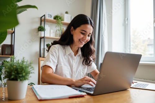 Happy woman working remotely on laptop in bright home office with plants and notebooks