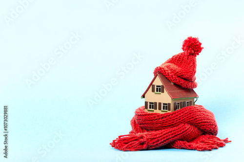 thermal insulation of buildings saves energy: miniature model house with red scarf and cap, blue background