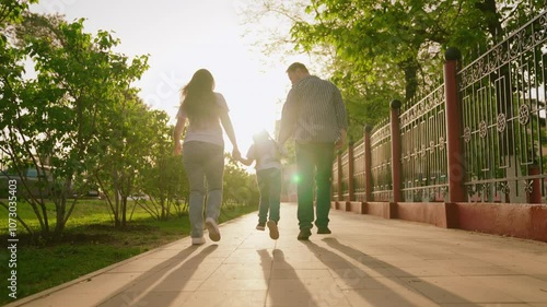 happy family. mother father child run through park sunset. mom dad kid fun running sun. view from back. happy family park. chidhood dream. family walk with kid around city playing. run teamwork
