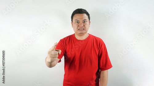 A young Indonesian man wearing a red t-shirt with an angry face facing forward