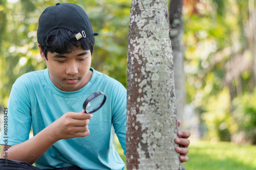 A young teenager holds a magnifying glass to look at outside skin or bark of the palm tree in school's botanical garden at weekend, science, botany, and nature study of young people concept. A young teenager holds a magnifying glass to look at outside skin or bark of the palm tree in school's botanical garden at weekend, science, botany, and nature study of young people concept.