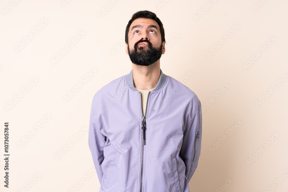 Caucasian man with beard wearing a jacket over isolated background and looking up Caucasian man with beard wearing a jacket over isolated background and looking up