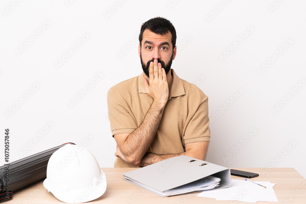 Caucasian architect man with beard in a table covering mouth with hand. Caucasian architect man with beard in a table covering mouth with hand.