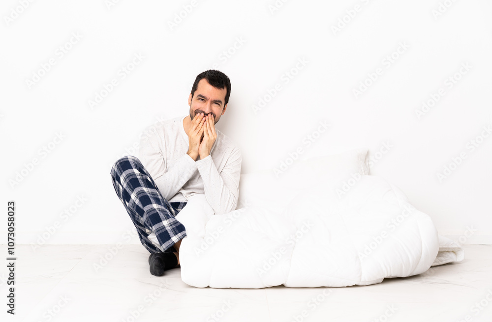 Caucasian man in pajamas sitting on the floor at indoors happy and smiling covering mouth with hands Caucasian man in pajamas sitting on the floor at indoors happy and smiling covering mouth with hands