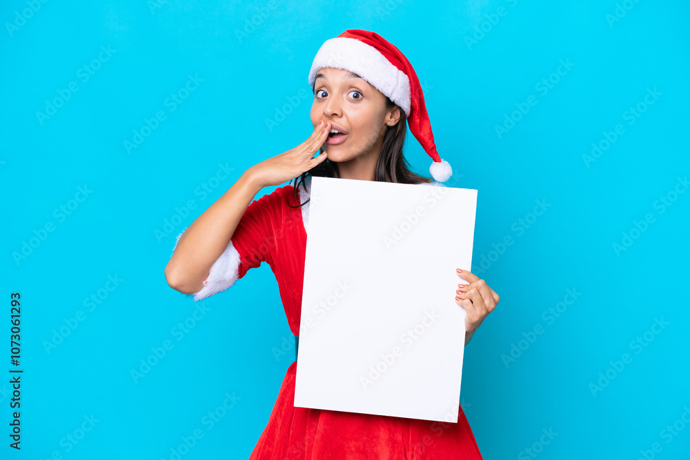 Young hispanic woman dressed as mama noel isolated on white background holding an empty placard with surprised expression Young hispanic woman dressed as mama noel isolated on white background holding an empty placard with surprised expression