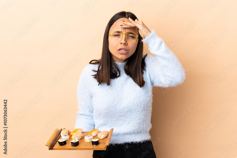Young brunette mixed race woman holding sushi over isolated background looking far away with hand to look something Young brunette mixed race woman holding sushi over isolated background looking far away with hand to look something