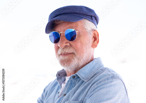 Portrait of handsome senior man on white background. Face of old man wearing blue sunglasses and cap outdoor. Retired relaxed man with white hair and beard in denim shirt